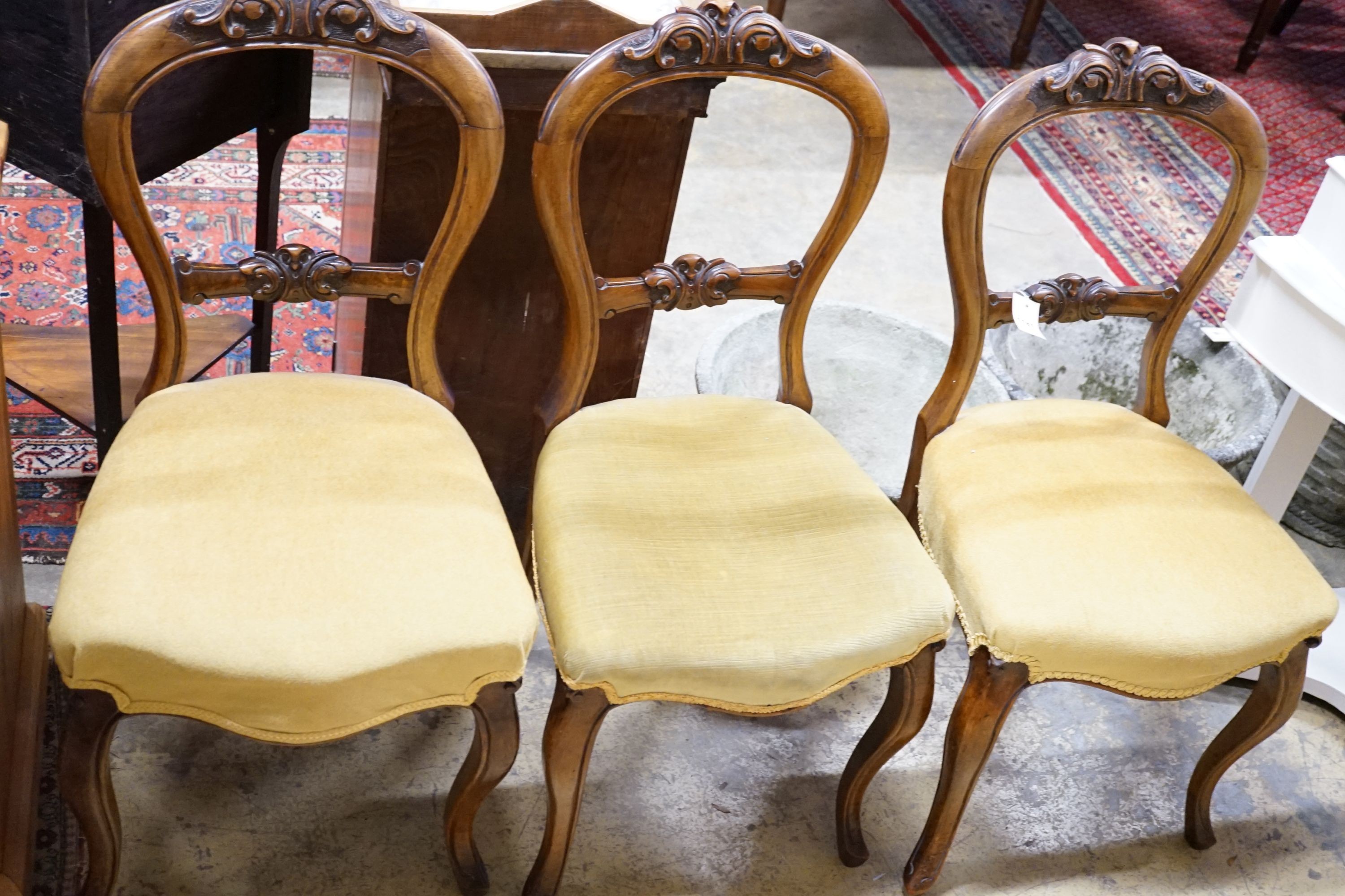 A set of three Victorian carved walnut balloon back saloon chairs stuff-over seats on cabriole legs